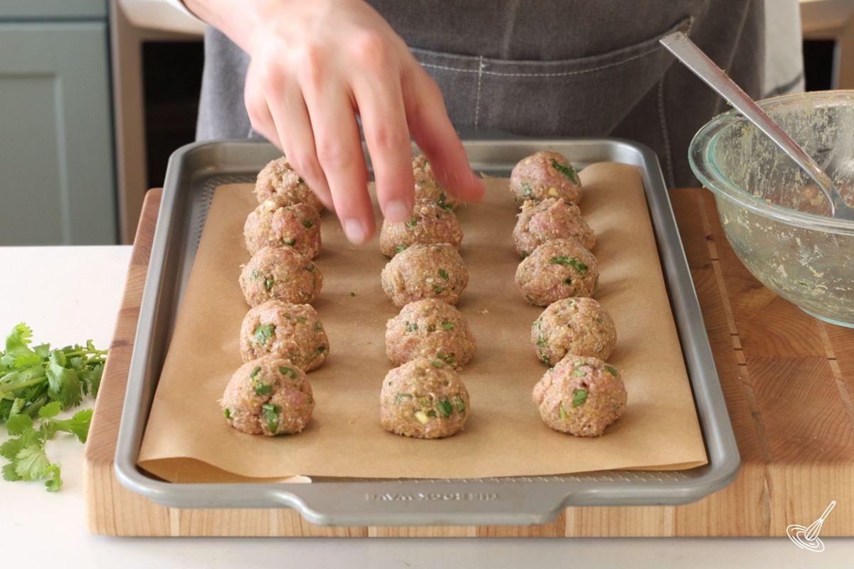 Someone placing meatballs on a cooking tray. 