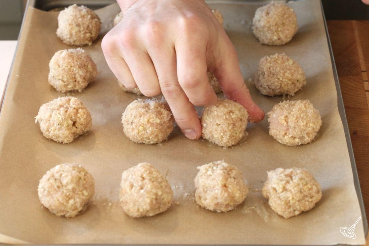 Someone placing shaped meatballs on a parchment paper lined tray.