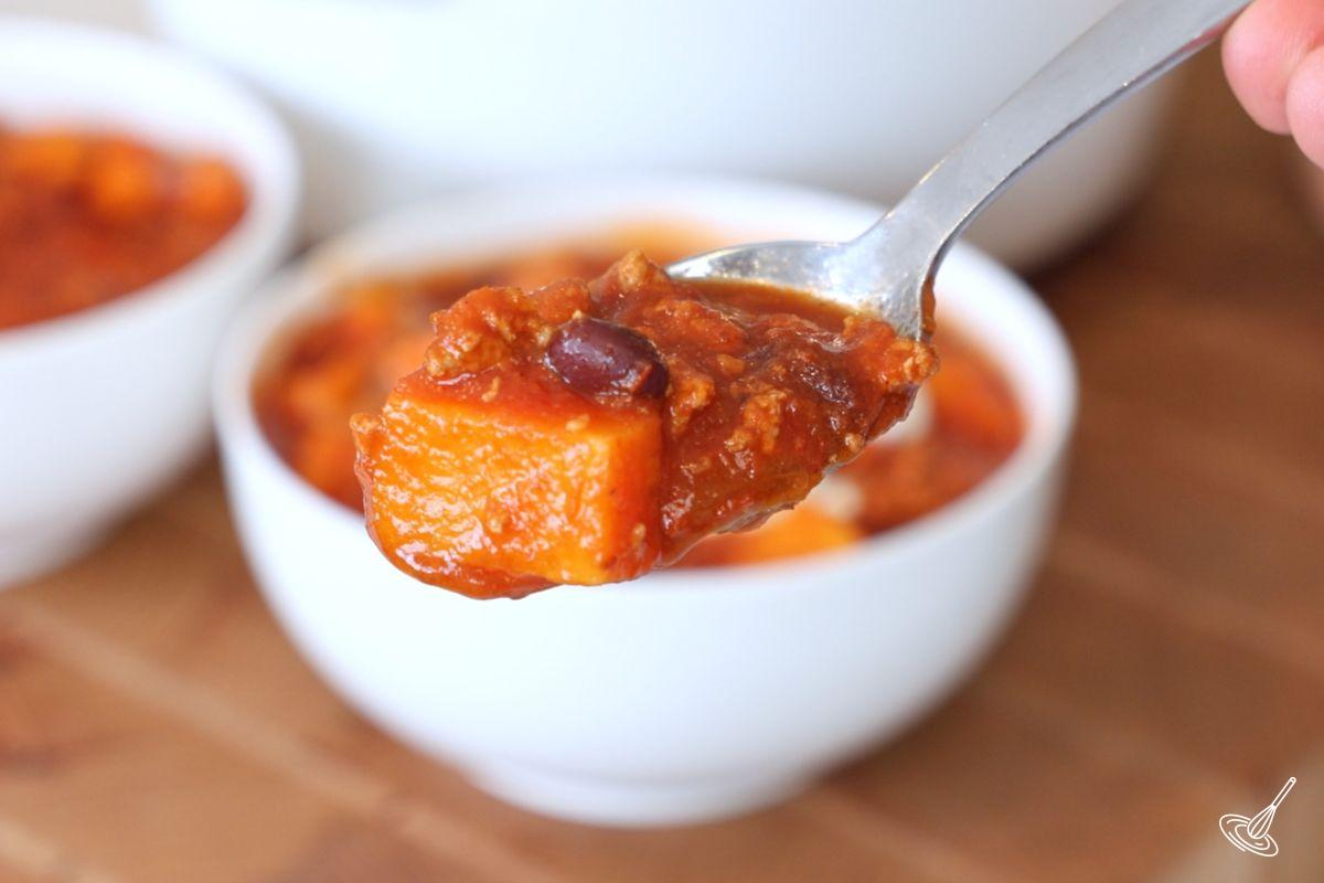 Une cuillère de chili à la dinde et à la patate douce tenue au-dessus d’un bol. 