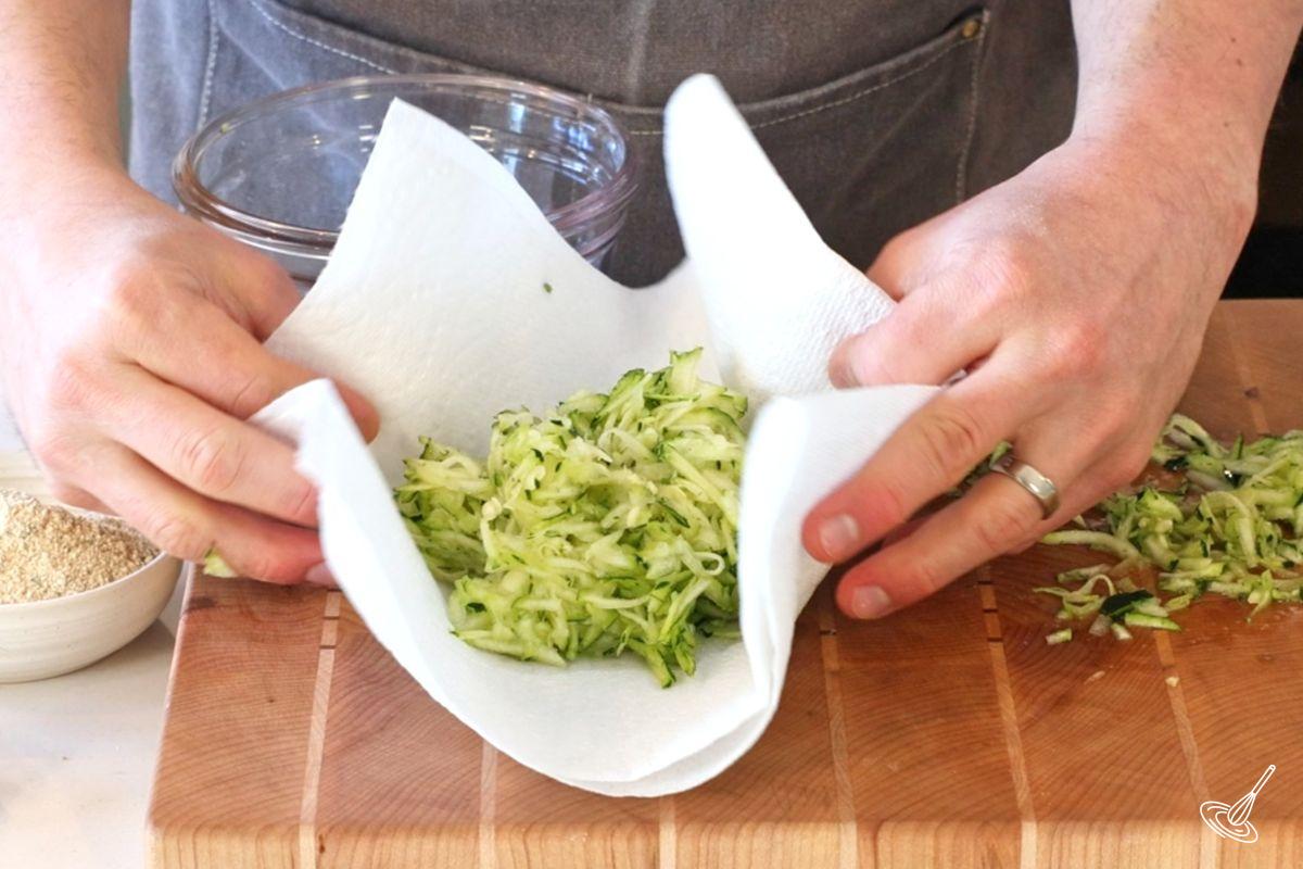 Quelqu’un utilise du papier absorbant pour essorer l’eau des courgettes râpées. 