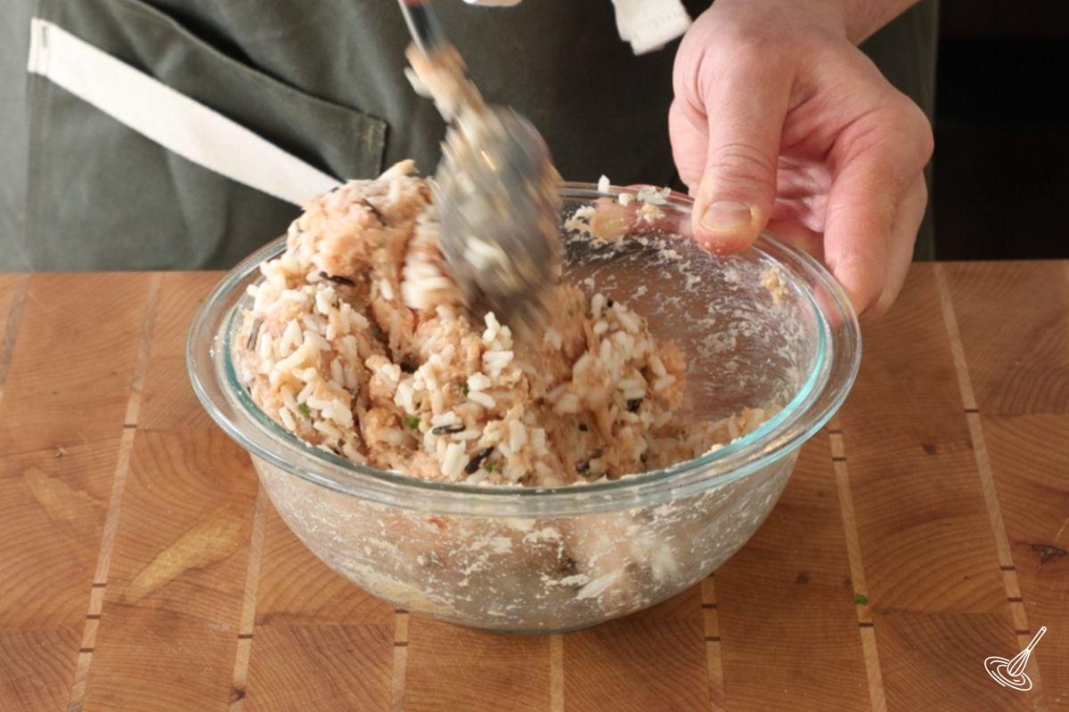Une personne utilise une cuillère pour incorporer le riz cuit au mélange de boulettes de viande.