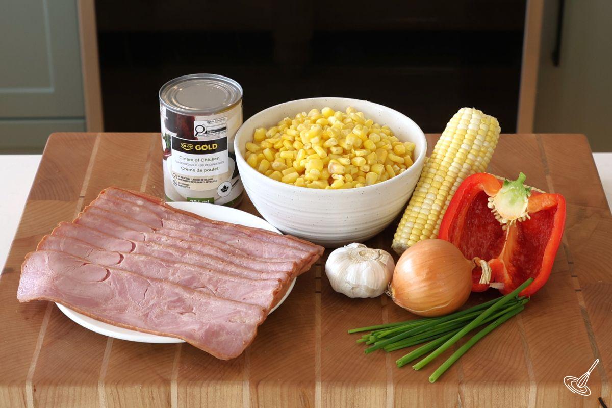 Ingredients on a cutting board, including turkey bacon, corn, a can of soup, and fresh vegetables.