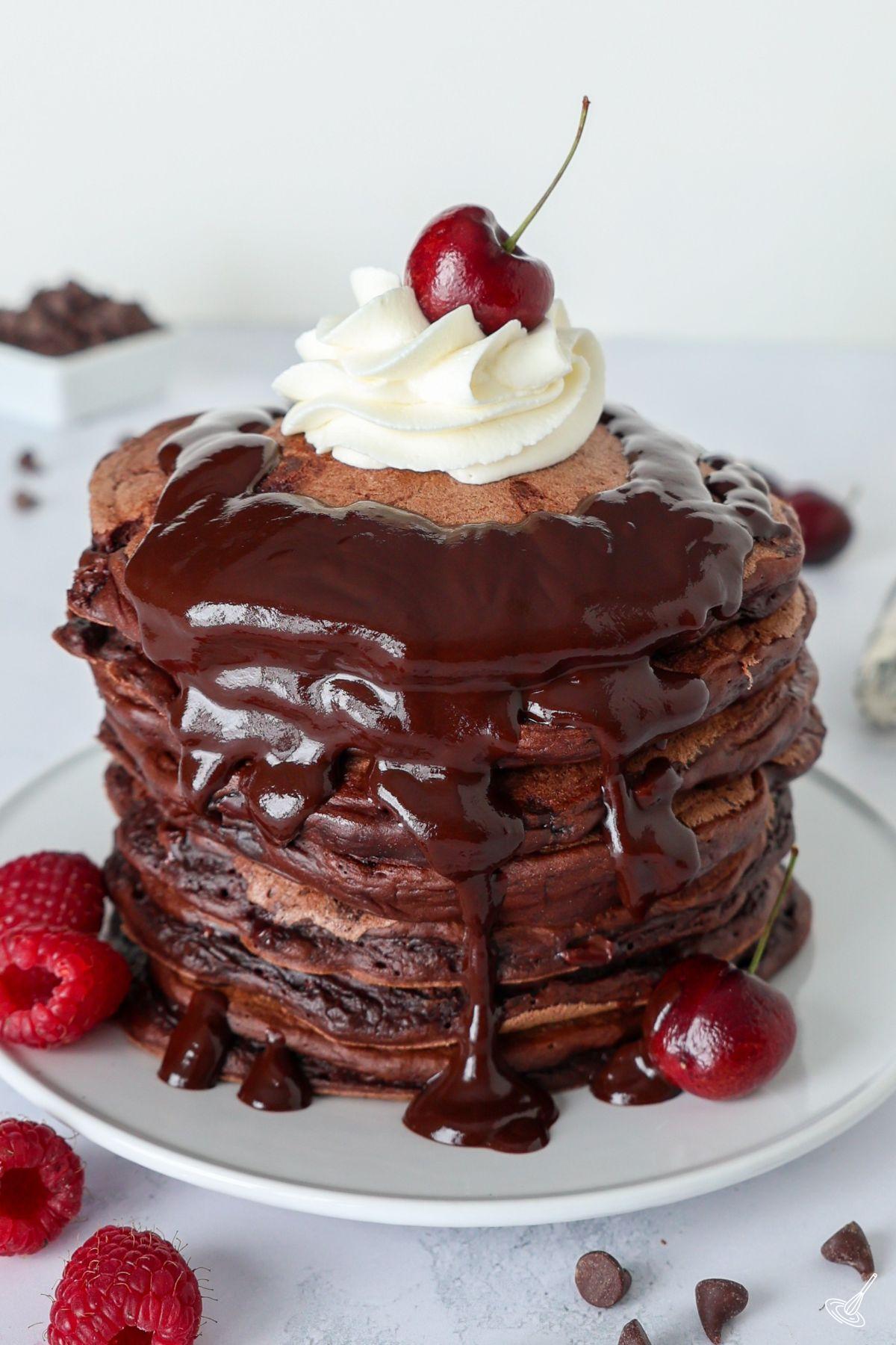 Une pile de pancakes double chocolat aux pépites de chocolat, nappés de sirop au chocolat et garnis d’une cerise sur le dessus.