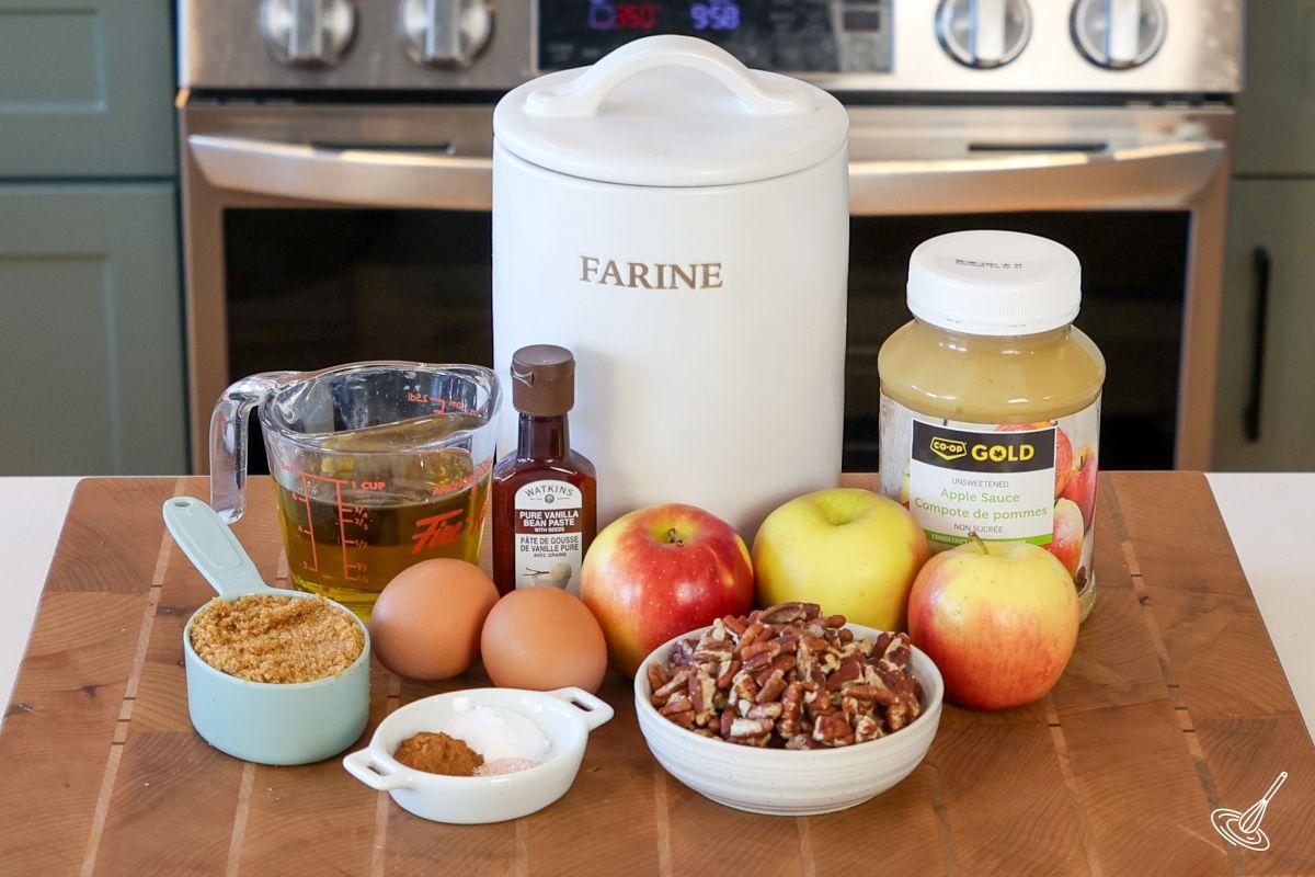 Ingredients on a cutting board including, apple sauce, flour, pecans, brown sugar, and apples.