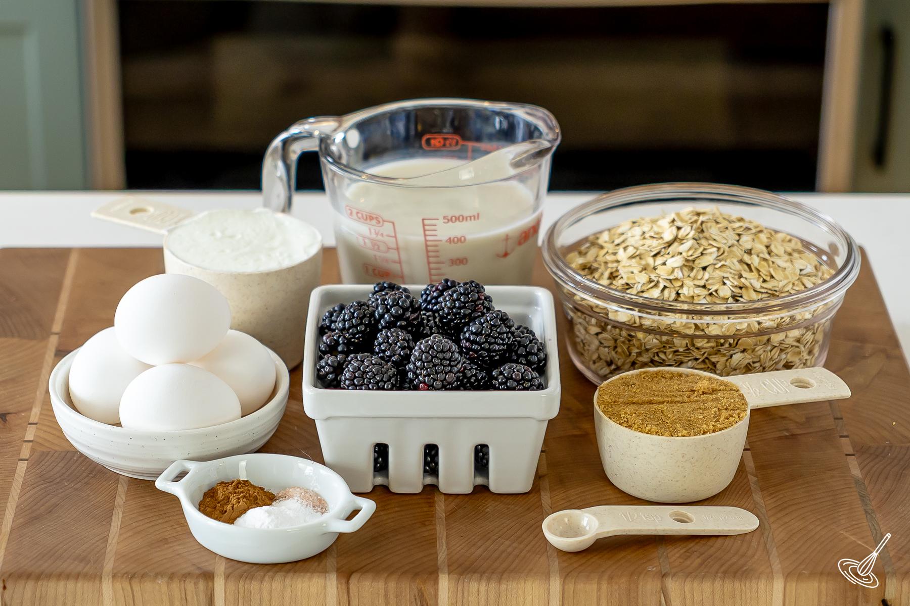 Ingrédients disposés sur une planche à découper, notamment des mûres, du lait, du yaourt, des flocons d'avoine et des œufs. 