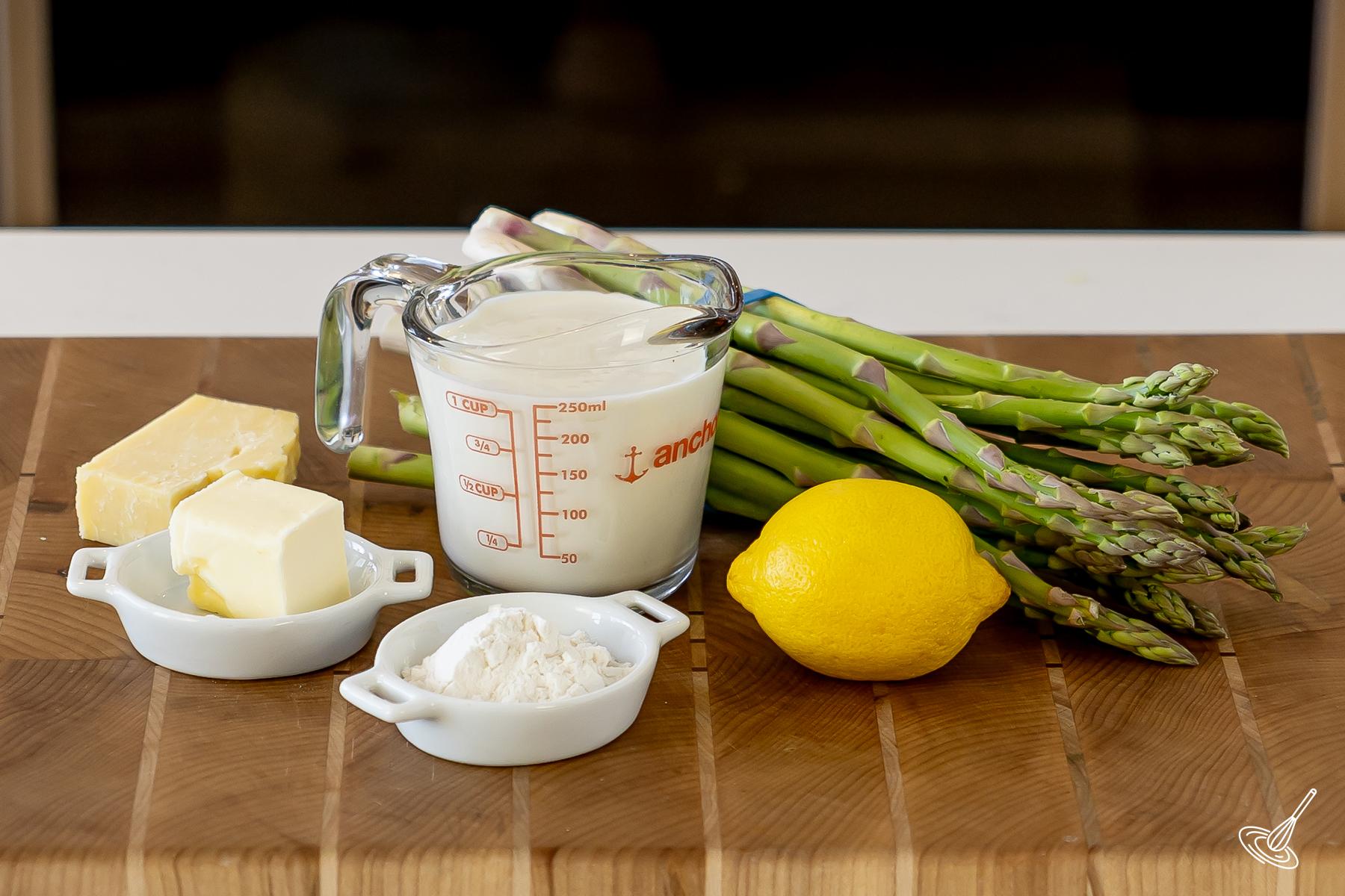Ingredients on a cutting board, including milk, butter, flour, lemon, and asparagus.