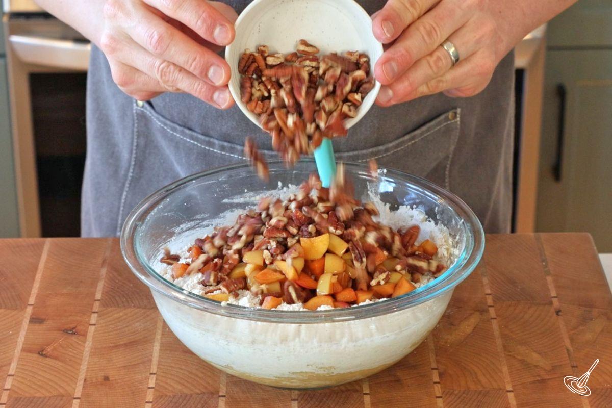 Someone adding pecan pieces and chopped apples to a bowl of cake batter.