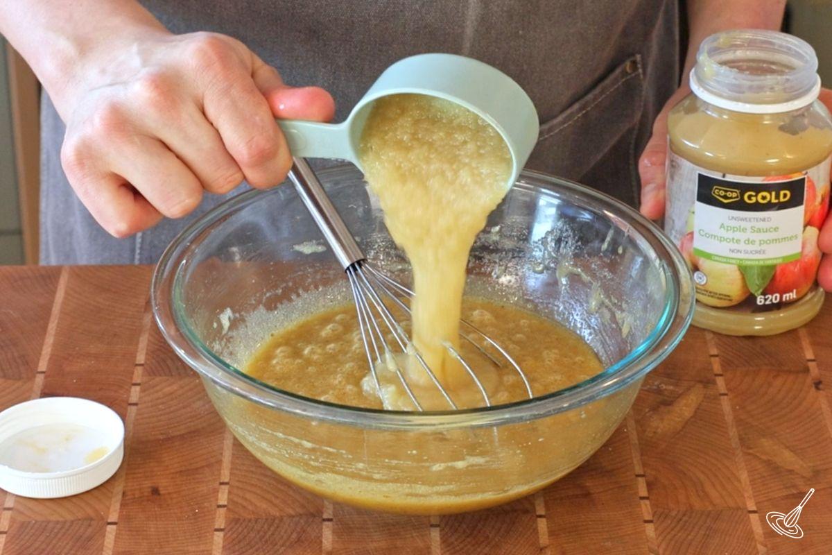Someone adding apple sauce to a bowl of eggs and oil.