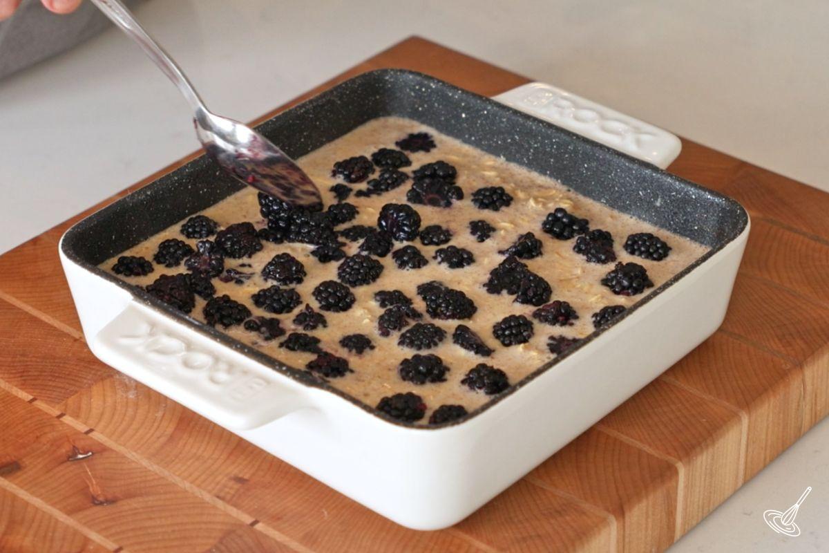 Quelqu'un qui ajoute des mûres à un plat de gruau cuit au four.