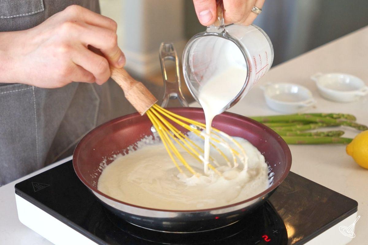 Someone whisking milk into a frying pan of cream sauce.