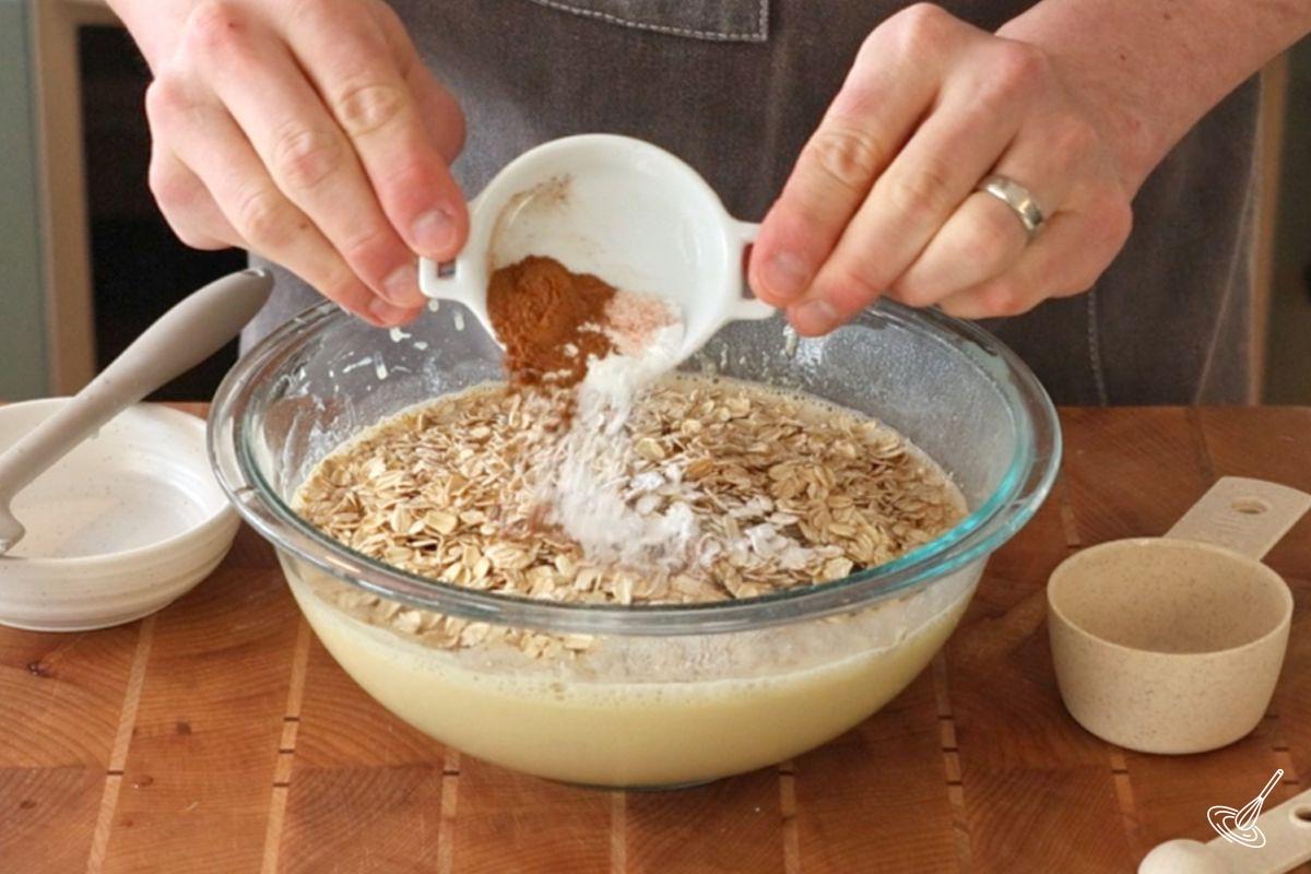 Quelqu'un qui ajoute des flocons d'avoine et des épices dans un bol.