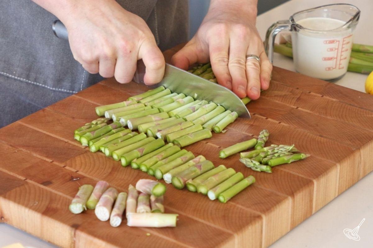 Someone using a knife to cut asparagus into 2 inch pieces. 