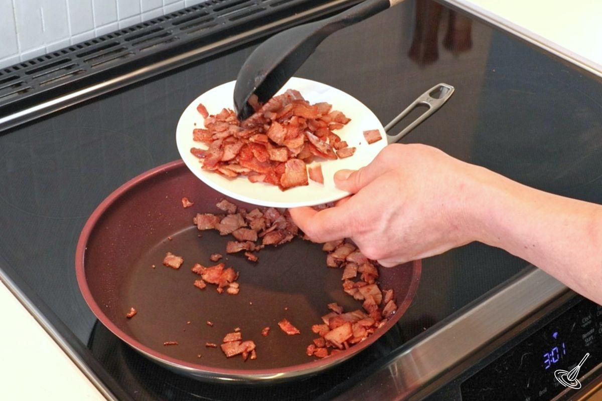 Someone removing crispy bacon from the pan and onto a plate.