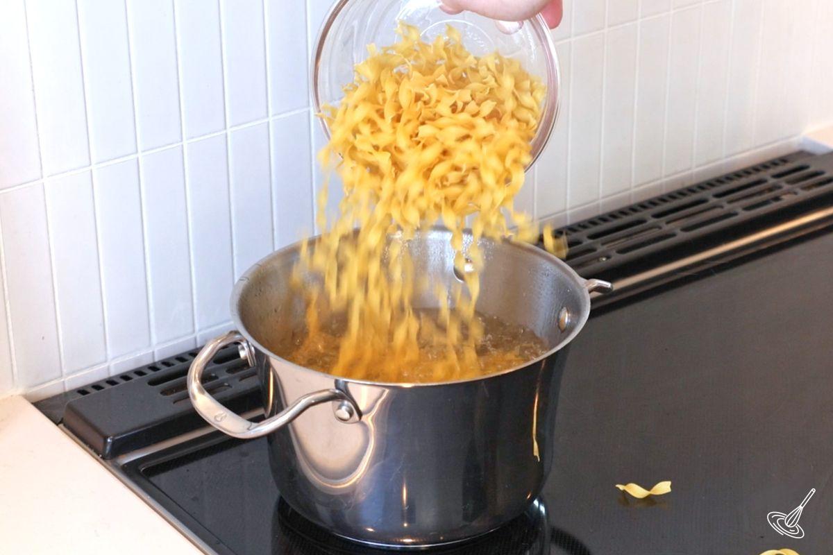 Quelqu'un qui ajoute des nouilles aux œufs à une casserole d'eau bouillante.