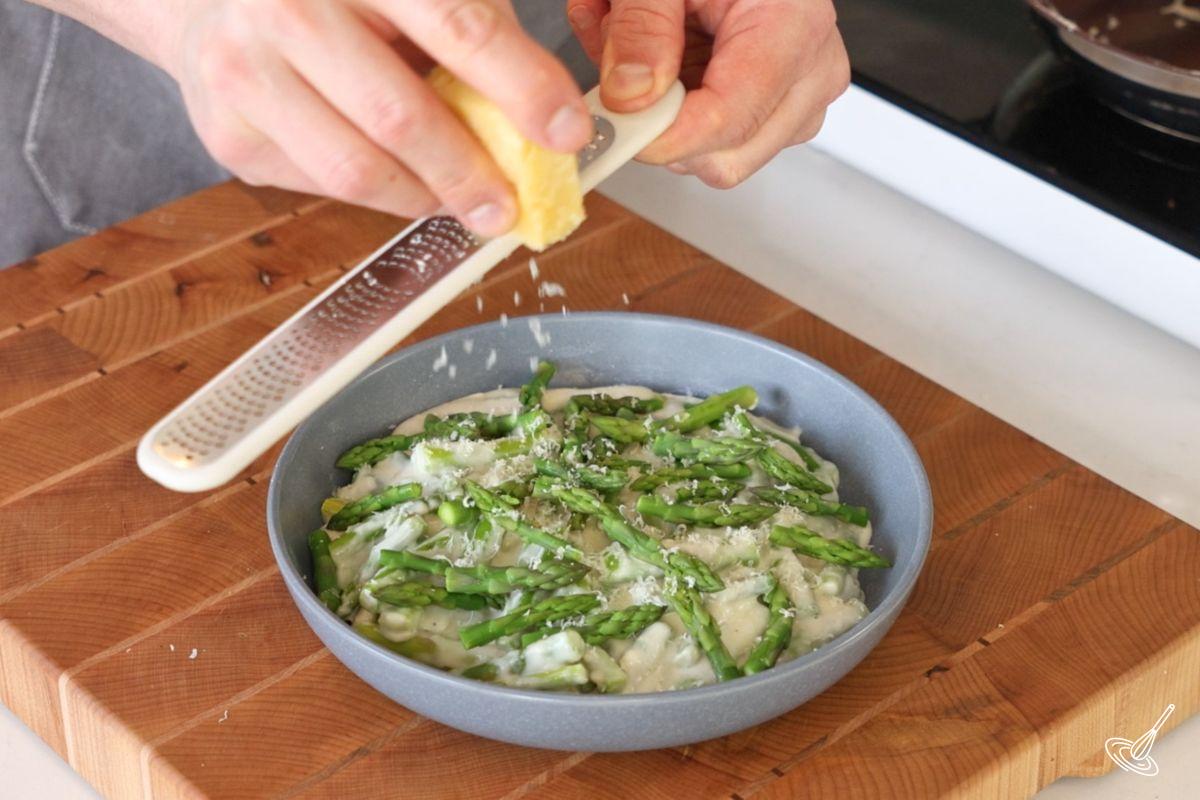Someone grating parmesan cheese over a dish of Creamed Asparagus.