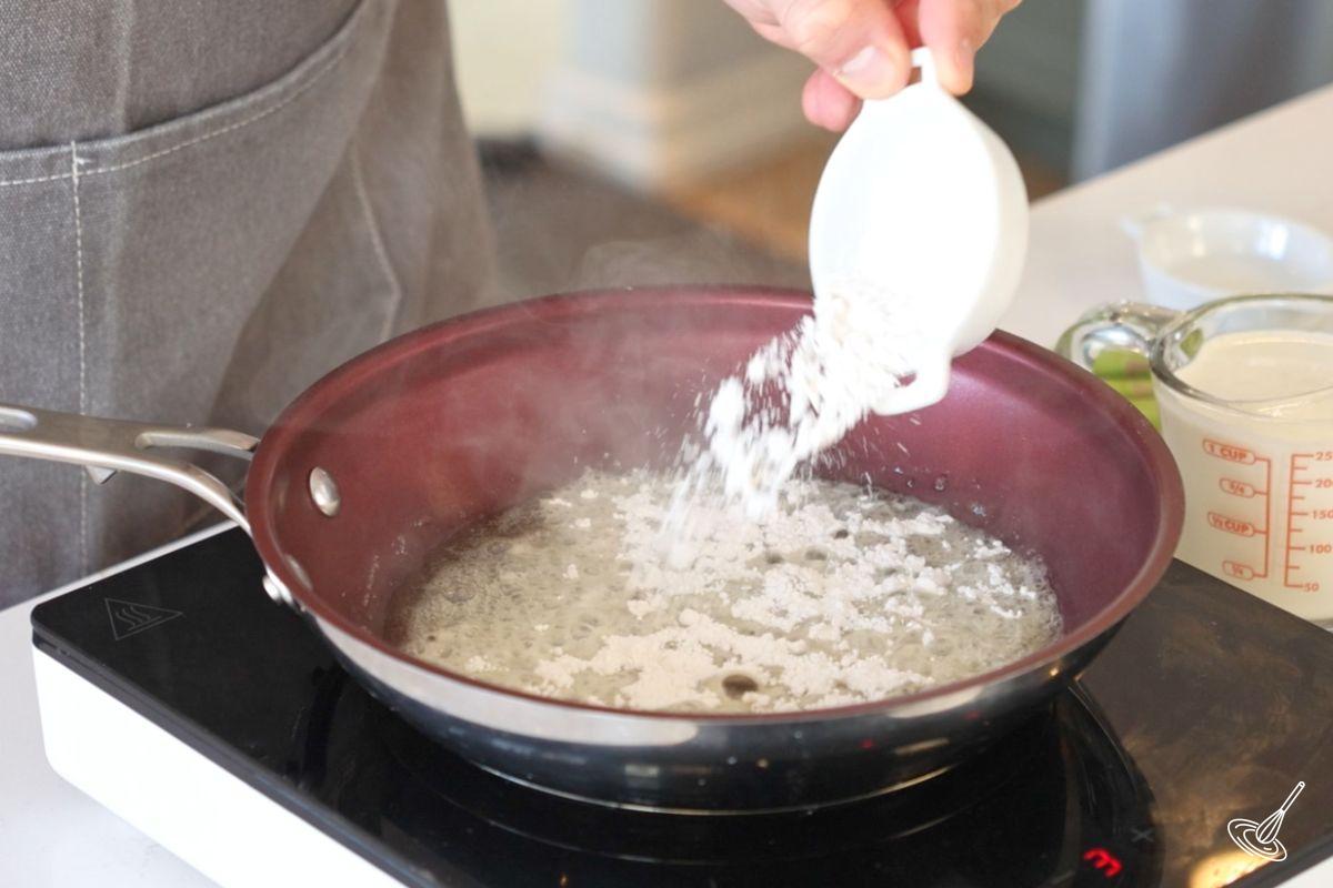 Someone adding flour to melted butter in a frying pan. 