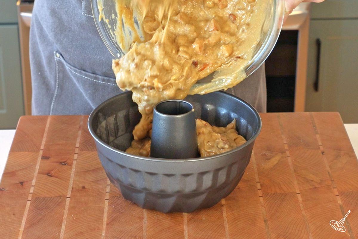 Someone pouring apple pecan cake batter to a bundt pan.