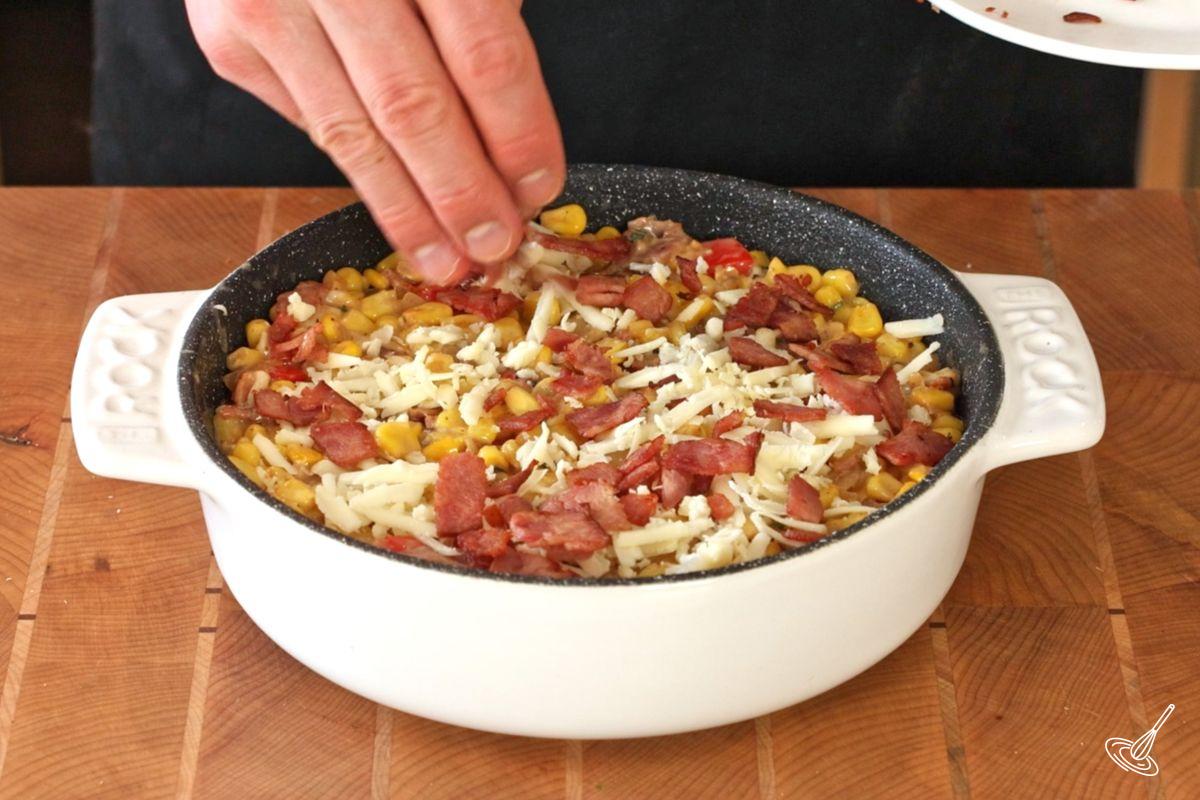 Someone garnishing the turkey bacon creamed corn casserole with grated cheese before baking.