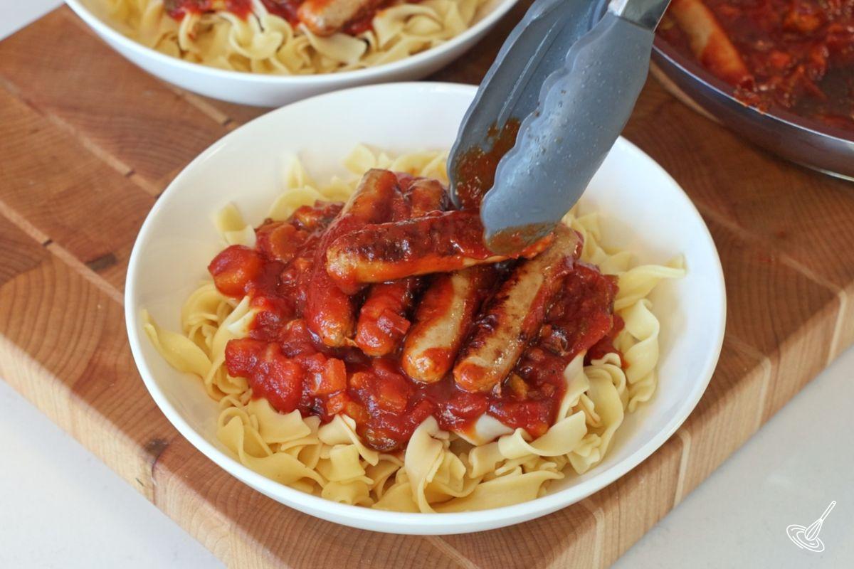 Quelqu'un qui dépose des saucisses de dinde cuites sur des nouilles aux œufs avec de la sauce chili. 