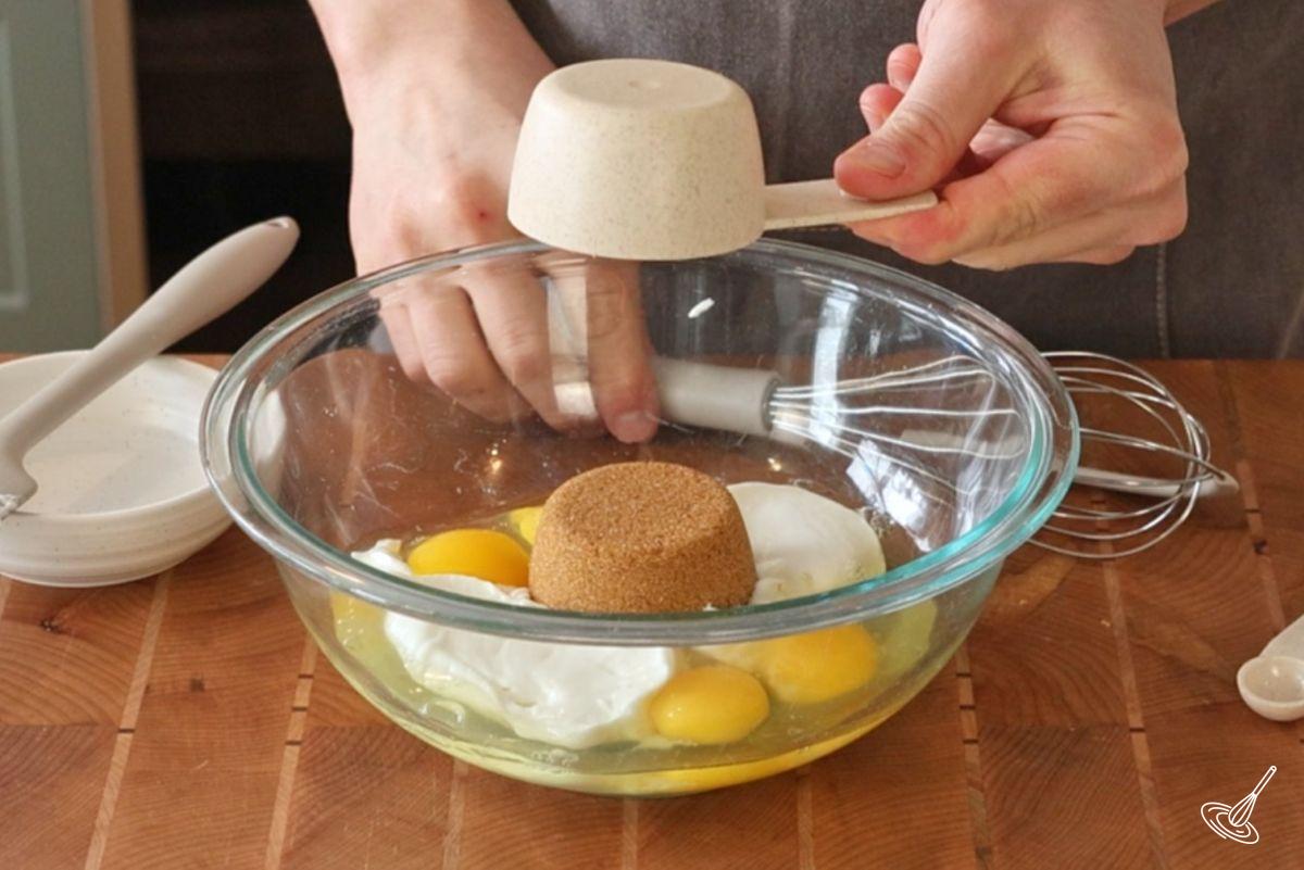 Quelqu'un qui ajoute du sucre brun à un bol d'œufs et de yaourt. 