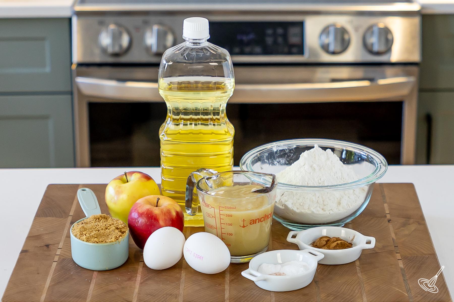 Ingredients on the kitchen counter, including canola oil, flour, apple sauce, apples, and brown sugar. 