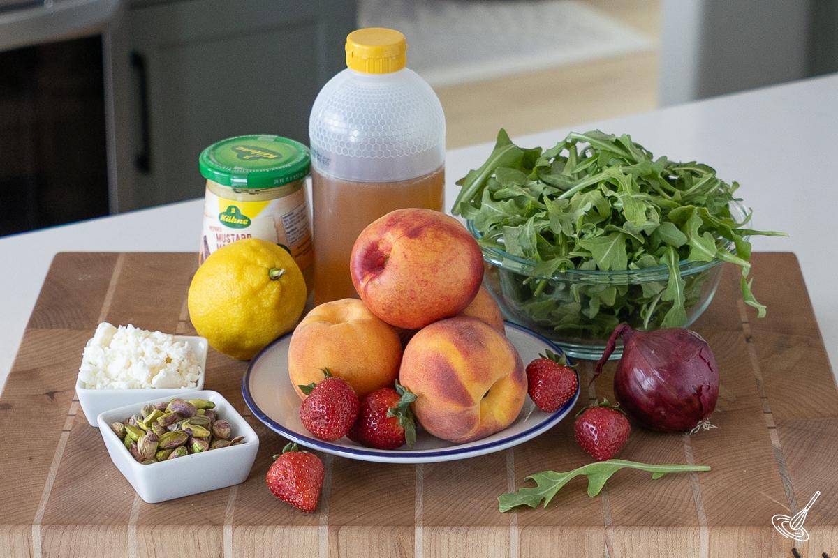 Ingredients on a cutting board, including peaches, arugula, honey, and a lemon. 
