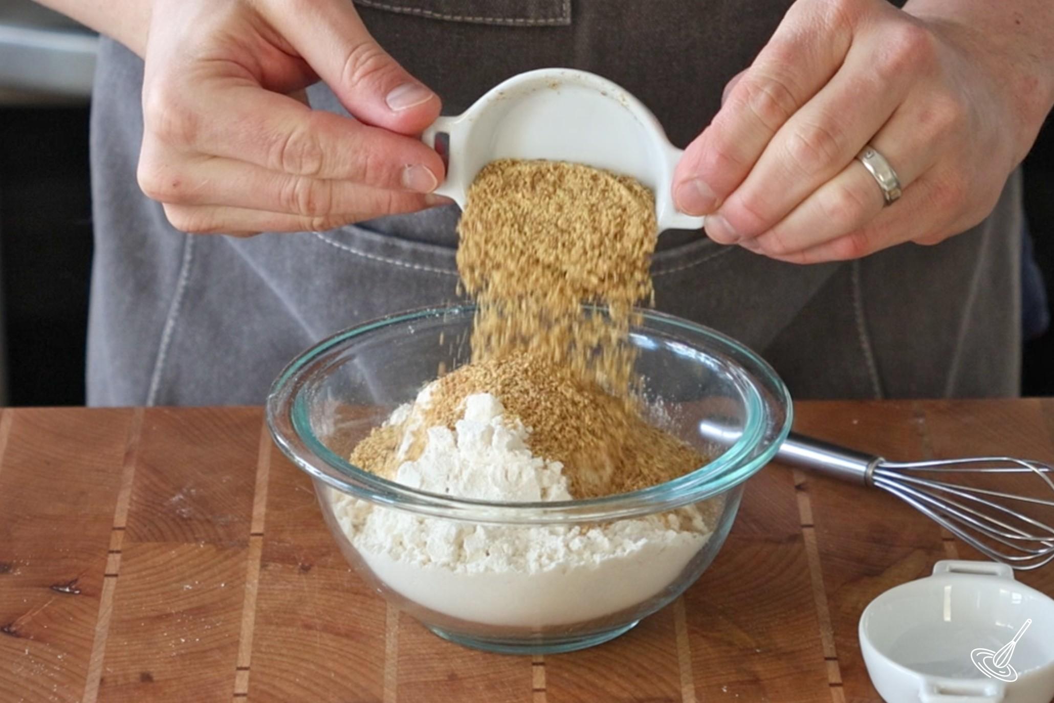 Quelqu’un ajoute des graines de lin moulues dans un bol de farine.