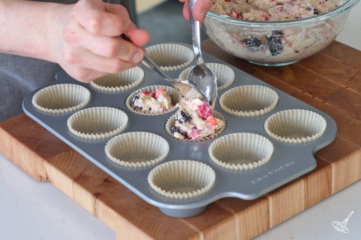 Quelqu’un dépose de la pâte à muffins dans le moule à muffins à l’aide d’une cuillère.