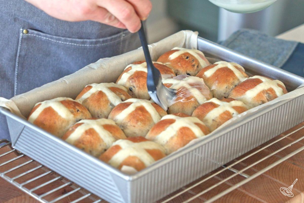 Someone brushing lemon glaze on the blueberry lemon hot cross buns. 