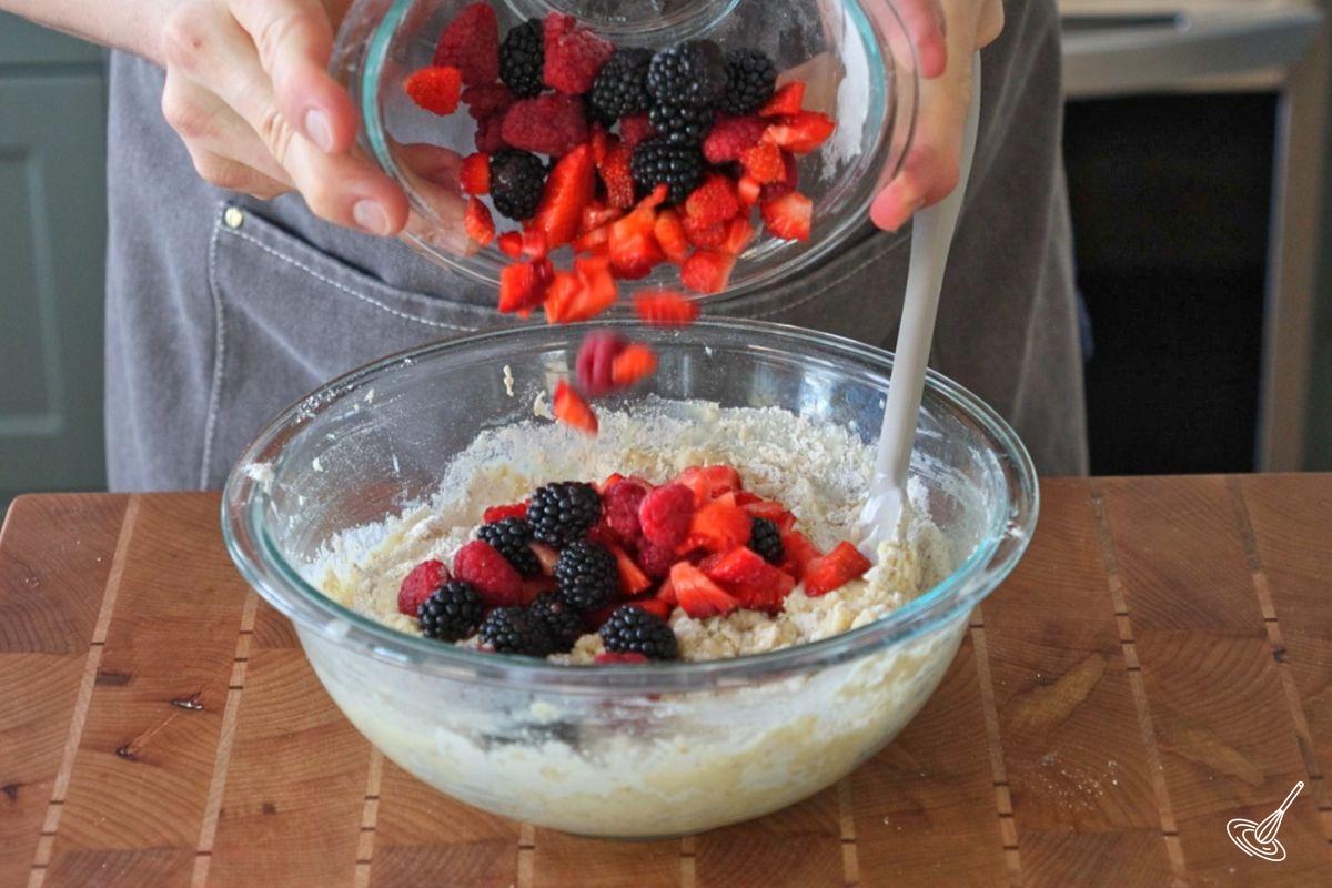 Quelqu’un ajoute des petits fruits frais dans un bol de pâte à muffins.
