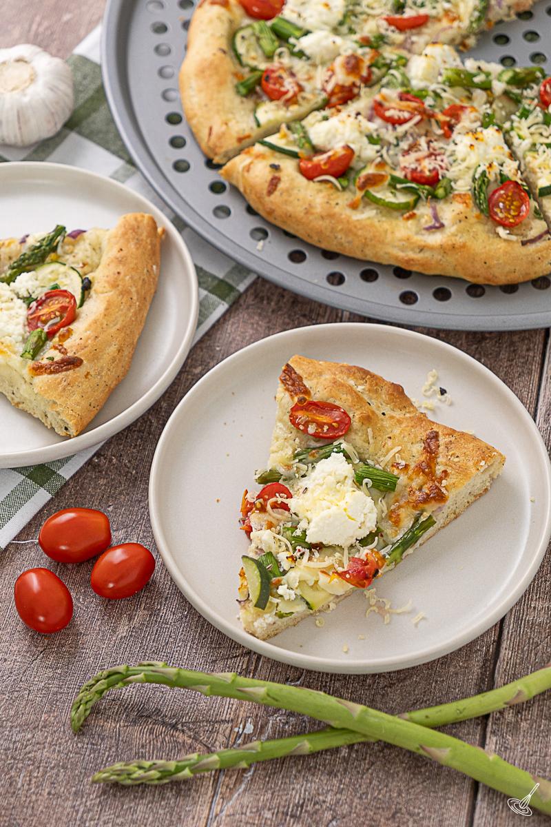 A couple slices of Primavera pizza on plates with the pizza on a pan. 