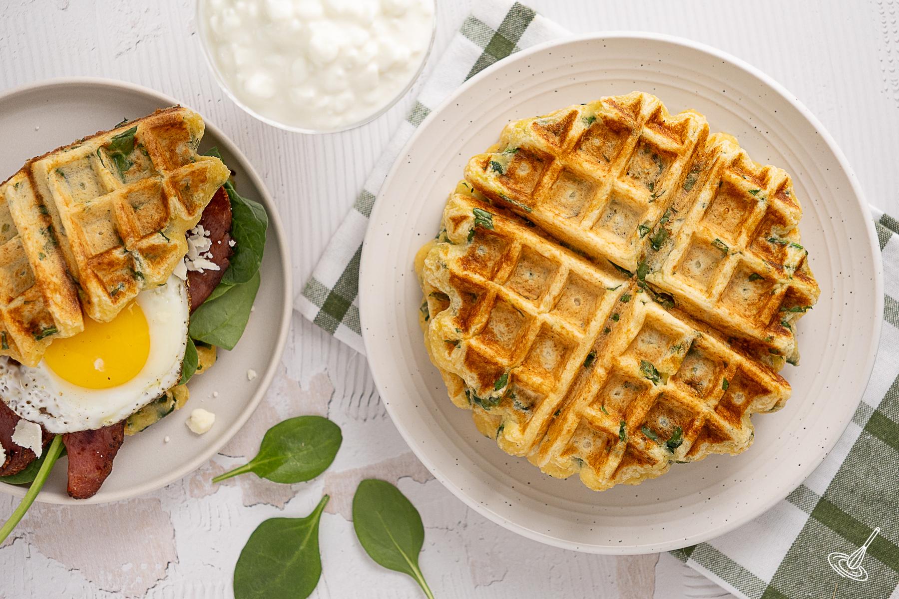 A plate of cottage cheese spinach waffles with a breakfast sandwich beside it. 