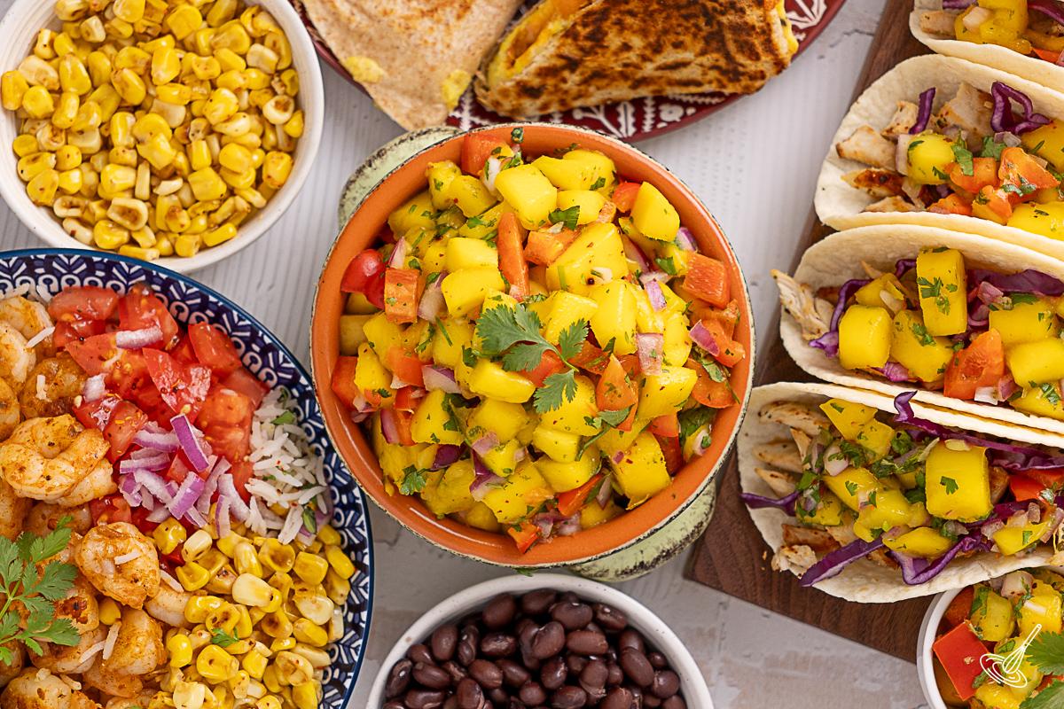 A serving bowl of Easy mango lime salsa on the table with other Mexican dishes. 