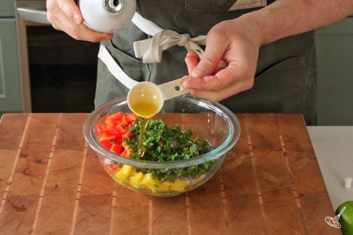 Someone adding olive oil into a bowl of mango salsa. 