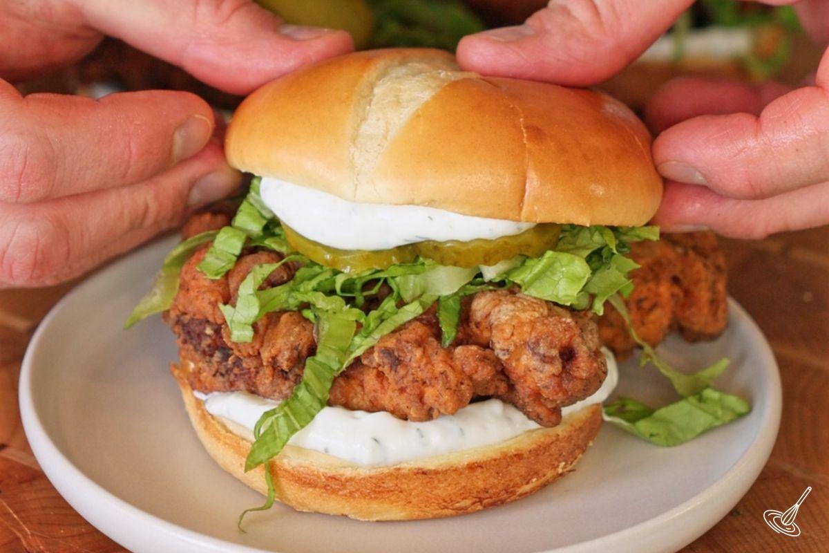 Someone placing the top bun on a Crispy Dill Turkey Sandwich. 