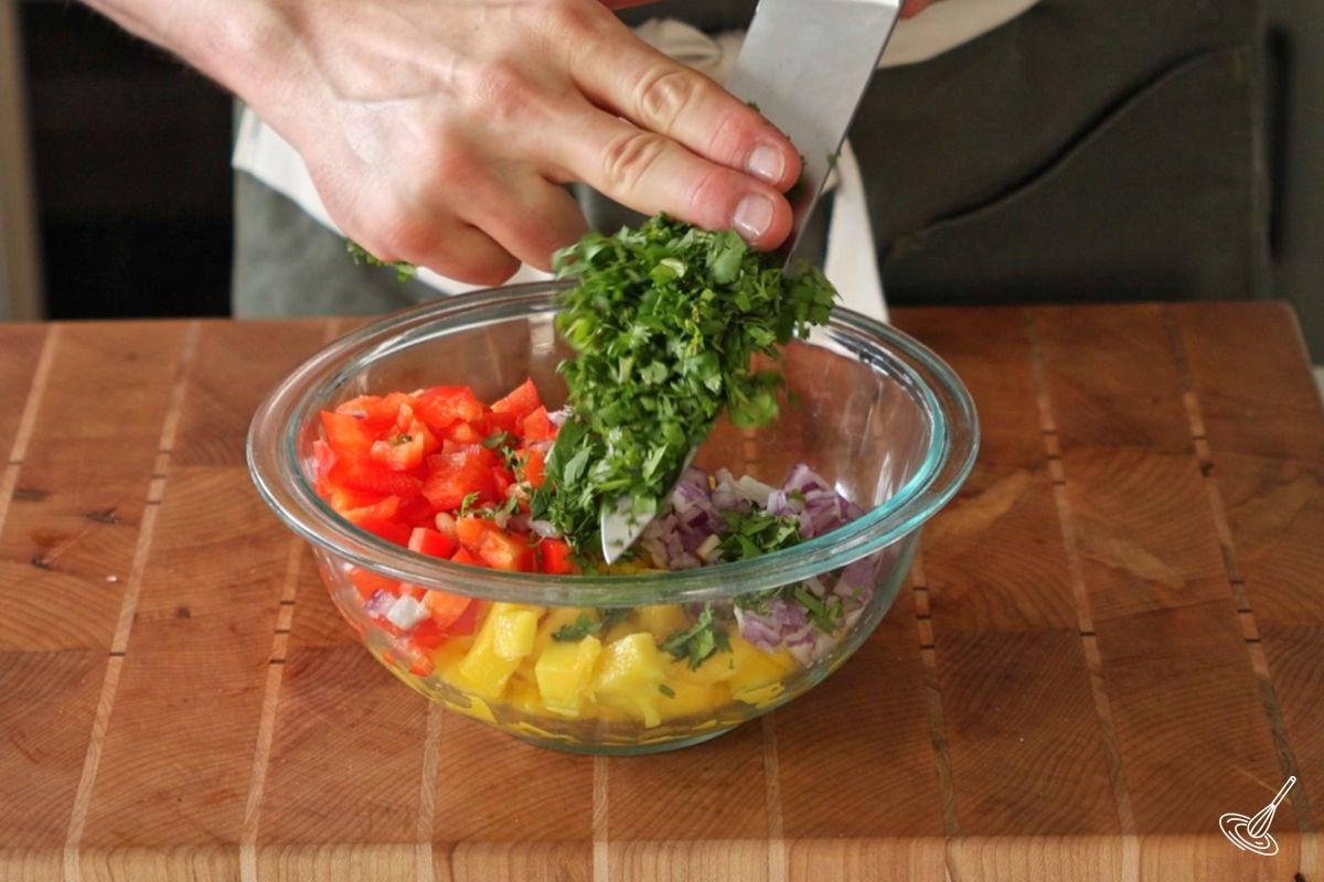 Someone adding chopped cilantro into a bowl of mango salsa. 