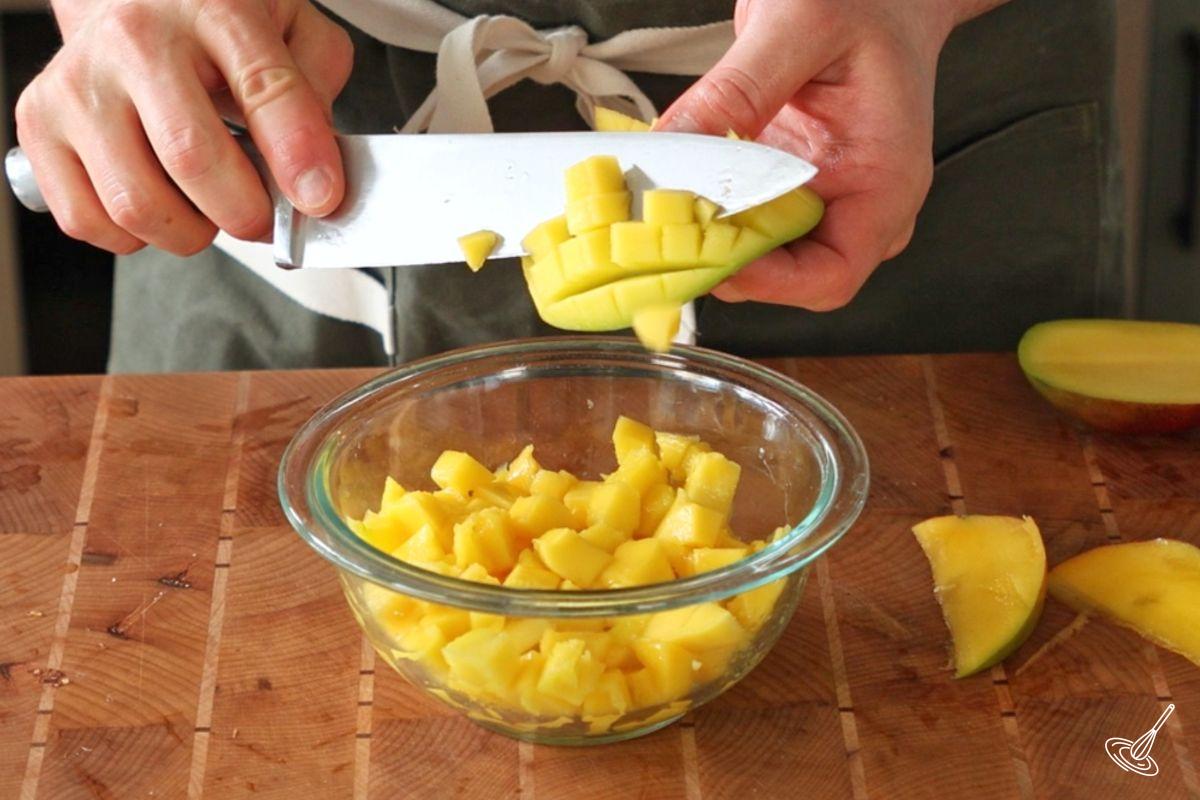 Someone cutting cubes of mango into a bowl.