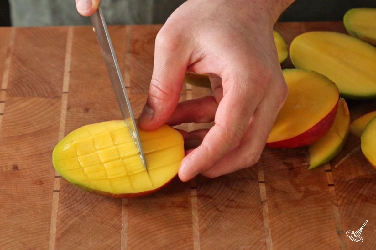 Someone using a knife to score the inside of a slice of mango. 