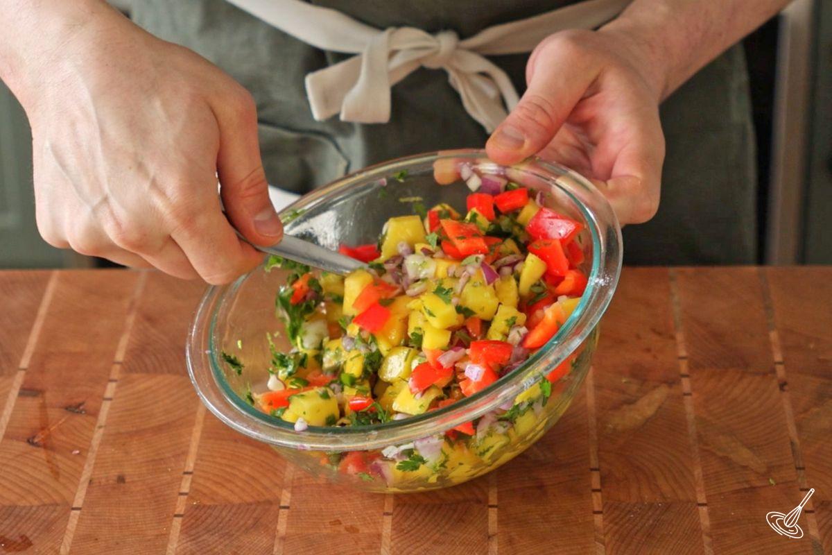 Someone using a spoon to stir a bowl of easy mango lime salsa. 