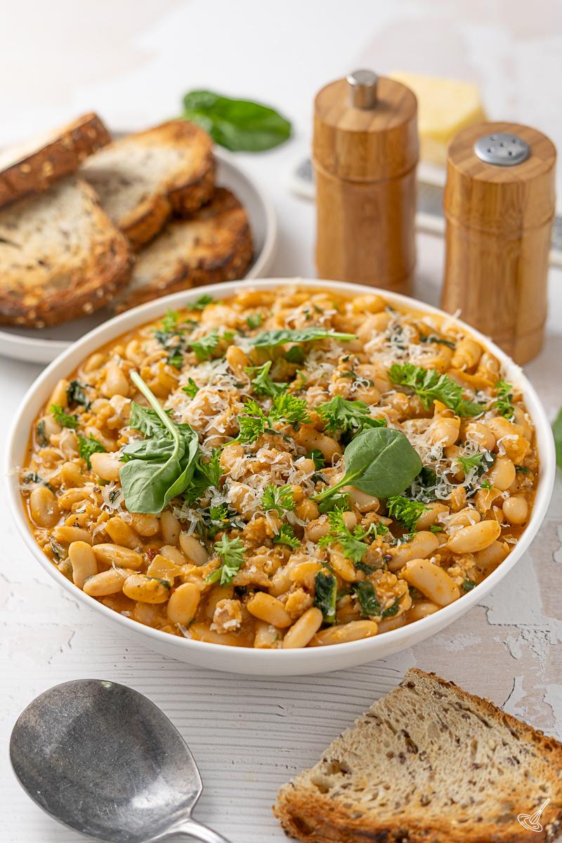 A bowl of Creamy White Bean and Spinach Sausage Skillet with a plate of toasted bread.